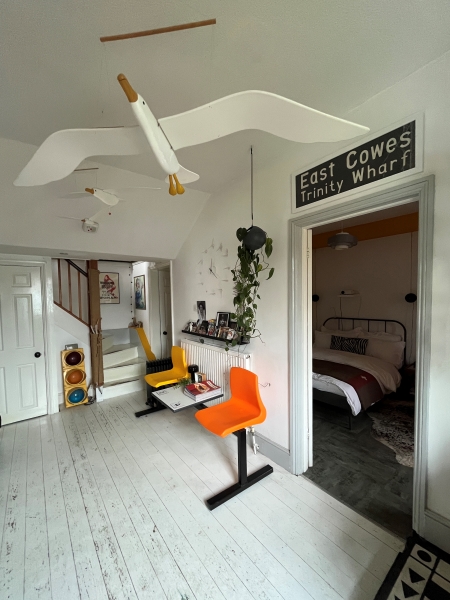 White entrance hall to Spike’s home, which includes 1980s destination sign for East Cowes, working American traffic light, and a white wooden bird model in flight hanging from the ceiling.